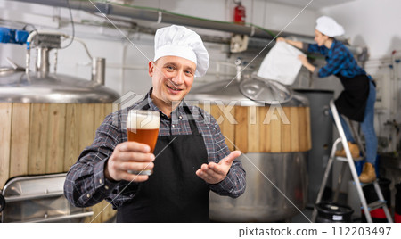 Happy brewery owner inviting to tasting amber beer 112203497