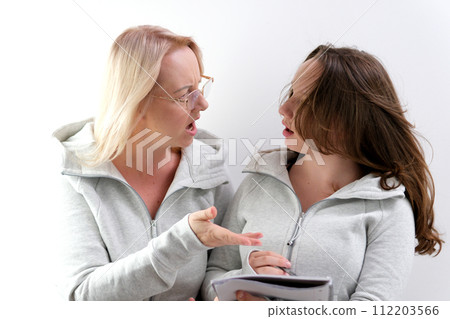 mom and daughter doing homework, woman wearing glasses, girl trying to write, they are laughing, smiling, spending pleasant time, explaining to child, surprise, pointing with hand at notepad, notebook mom and daughter doing homework, woman wearing glasses, girl trying to write, they are laughing, smiling, spending pleasant time, explaining to child, surprise, pointing with hand at notepad, notebook 112203566