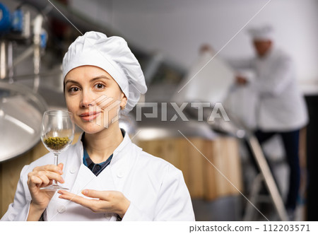 Successful female brewmaster showing hop pellets in glass 112203571