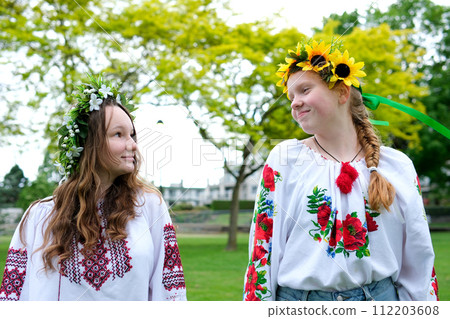 Midsummer. Two girls in Slavic clothes talking while sitting by the fire 112203608