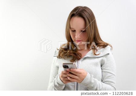Portrait of tense concentrated female teenager with very long brown hair playing game on her cell phone being winner gesturing in joy over white background. Concept of emotions Portrait of tense concentrated female teenager with very long brown hair playing game on her cell phone being winner gesturing in joy over white background. Concept of emotions 112203628