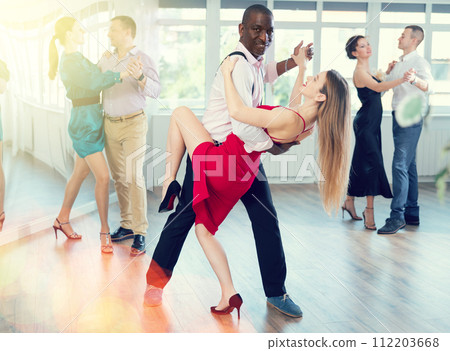 Elegant african american man performing kizomba paired with attractive woman in red in studio class setting 112203668