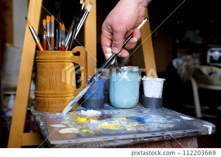 artist paints a picture of oil paint brush in hand with palette closeup artist paints a picture of oil paint brush in hand with palette closeup 112203669