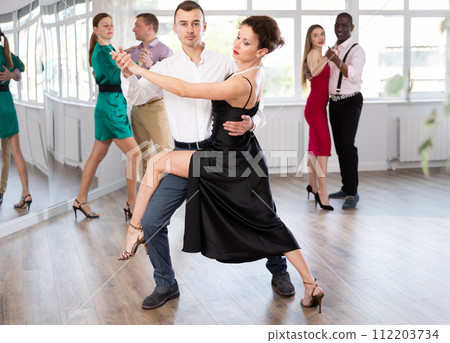 Elegant couple performs an expressive tango in bright, modern dance studio during group class 112203734