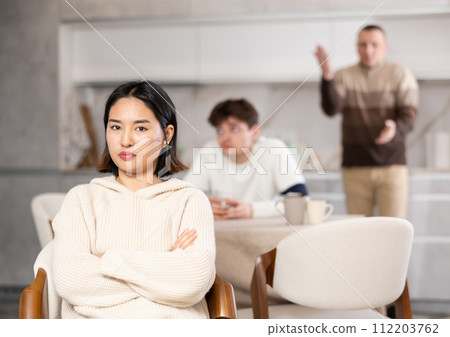 Upset woman not talking after disagreement with father and husband standing behind 112203762