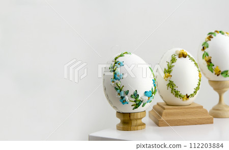 close-up of three white eggs on stands embroidery with ribbons on an eggshell example technology beautiful ornament handmade Easter holiday easter eggs decoration drawing on eggs as a gift close-up of three white eggs on stands embroidery with ribbons on an eggshell example technology beautiful ornament handmade Easter holiday easter eggs decoration drawing on eggs as a gift 112203884