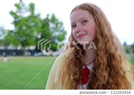 A young woman smiling. red-haired girl in a yellow sweater in nature Green grass white sky loose long hair of a young woman A young woman smiling. red-haired girl in a yellow sweater in nature Green grass white sky loose long hair of a young woman 112203916