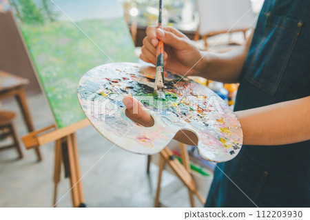 Close-up Art student's hand using a paintbrush to mix colors on a palette in hand to watercolor painting on canvas doing some art projects Close-up Art student's hand using a paintbrush to mix colors on a palette in hand to watercolor painting on canvas doing some art projects 112203930