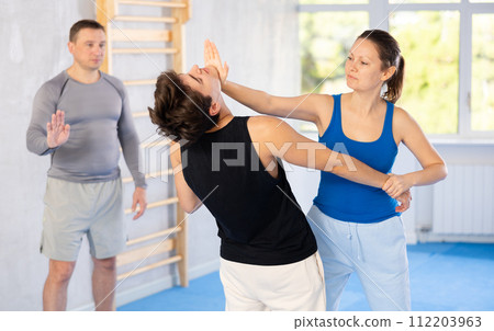 Self-defense class - a woman practices blows to the head of an attacking man under the guidance of trainer Self-defense class - a woman practices blows to the head of an attacking man under the guidance of trainer 112203963