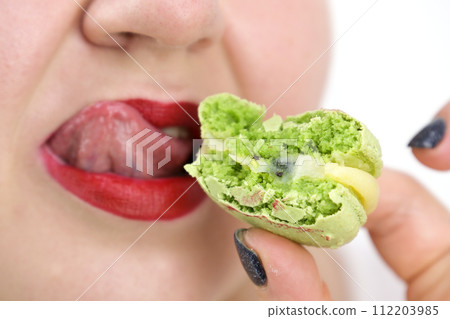 cropped view of woman eating sweet green macaron, isolated on white cropped view of woman eating sweet green macaron, isolated on white 112203985