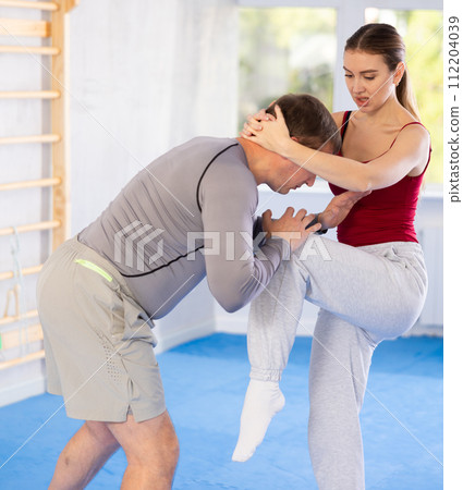 Young woman kicks attacking man - self-defense training in ring 112204039
