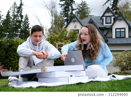 Outdoor picnic on green grass open box with knitting needle pleasant emotions fun pastime teenagers first date sit near the house private sector show thumb up tasting pizza delicious food surprise joy 112204093
