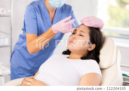 Professional cosmetologist hands in rubber gloves performing lips enhancement treatment to female client, making injection of lip fillers Professional cosmetologist hands in rubber gloves performing lips enhancement treatment to female client, making injection of lip fillers 112204105