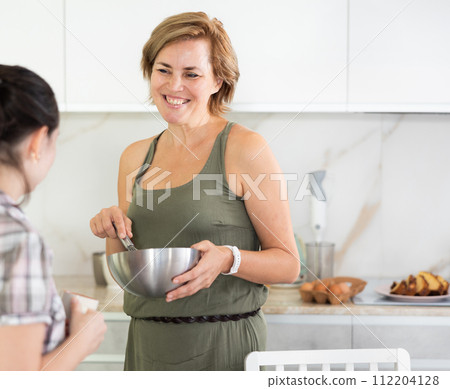 Two women are cooking lunch and chatting nicely in kitchen 112204128