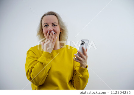 Afraid funny caucasian woman wearing white T-shirt over white background holding telephone and bitting nails Afraid funny caucasian woman wearing white T-shirt over white background holding telephone and bitting nails 112204285