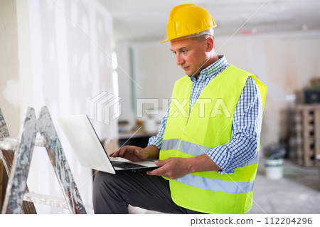 Man builder using laptop in construction site Man builder using laptop in construction site 112204296