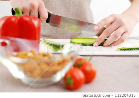 close-up beautiful female young hands cut cucumber with big knife glass dish beige background cooking delicious diet food kitchen Family hearth parsley selective focus grocery store cooking delivery 112204313