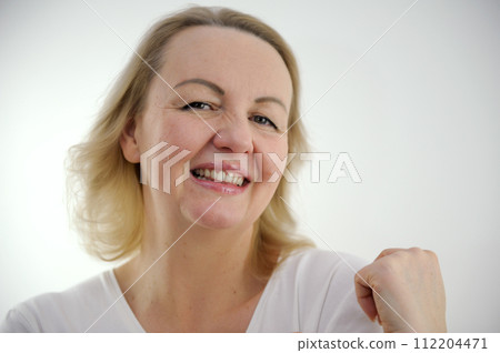 tenderness pleasure on face of sly look of sincere smile raised one shoulder up looks askance coquetry woman on white background pleasant product purchase excellent emotion white t-shirt fair hair 112204471