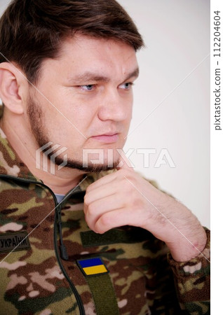 Ukrainian soldier leaned his head on hand and thought uniform inscription on jacket armed forces of Ukraine pain and sadness in his eyes. the war changed life. Russia attacked Ukraine 112204604
