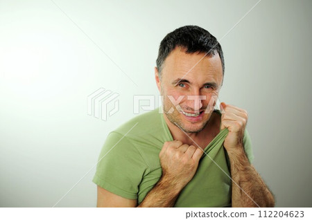 sly funny look adult unshaven man tears Green khaki T-shirt and bites his fingers 40-49 years Black hair at the temples gray Experience stress upset neurosis Studio white background sly funny look adult unshaven man tears Green khaki T-shirt and bites his fingers 40-49 years Black hair at the temples gray Experience stress upset neurosis Studio white background 112204623