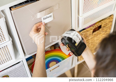 Woman mother applying paper sticker with name title on basket container clean out of childish toys 112204966