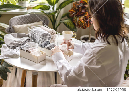 Unrecognizable woman sorting neatly folded linen cotton textile at container and basket on table Unrecognizable woman sorting neatly folded linen cotton textile at container and basket on table 112204968