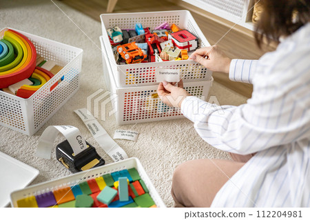 Woman clean out childish room sorting wooden and plastic toys use mobile label printer sticker title Woman clean out childish room sorting wooden and plastic toys use mobile label printer sticker title 112204981