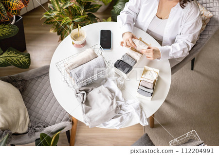 Unrecognizable woman sorting neatly folded linen cotton textile at container and basket on table Unrecognizable woman sorting neatly folded linen cotton textile at container and basket on table 112204991