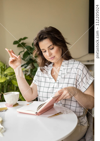 Smiling young business woman planning work making notes in paper diary at comfortable home 112205024