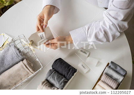 Woman hands cutting sticker tag scissors comfortable storage organizing linen textile in container 112205027