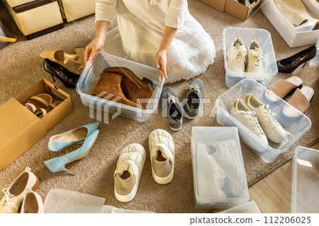 Woman arrangement shoes into plastic container and cardboard box seasonal storage organizing closeup 112206025