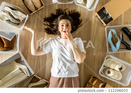 Woman surrounded by shoes in plastic container and cardboard box shopaholism and storage organizing Woman surrounded by shoes in plastic container and cardboard box shopaholism and storage organizing 112206035