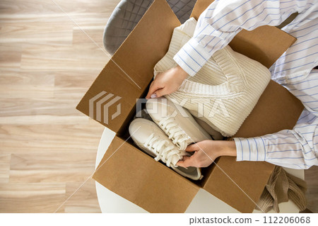 Woman packing clothes and shoes into cardboard box seasonal comfortable storage organize top view Woman packing clothes and shoes into cardboard box seasonal comfortable storage organize top view 112206068