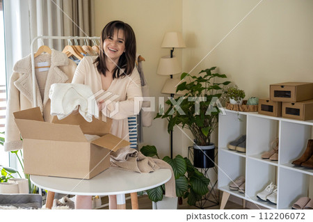 Woman putting seasonal warm clothes into cardboard box for donation and comfortable storage organize Woman putting seasonal warm clothes into cardboard box for donation and comfortable storage organize 112206072