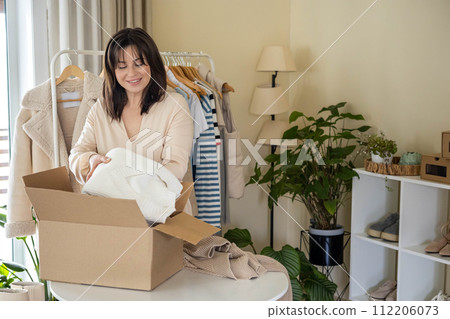 Woman putting seasonal warm clothes into cardboard box for donation and comfortable storage organize 112206073