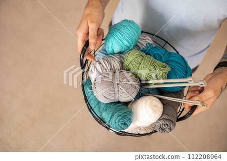 A man holds a large basket with colorful yarn. 112208964