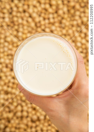 Woman's hand holding a glass of soybeans and soy milk Woman's hand holding a glass of soybeans and soy milk 112208995