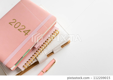 Pink coral colored diary for the year 2024 and many other diaries, pen, white background 112209015