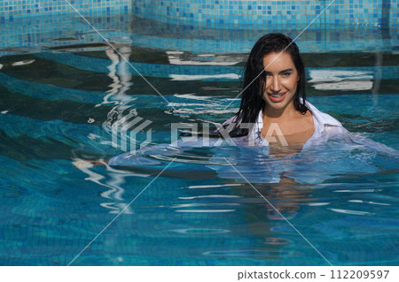 beautiful young sexy woman with vitiligo disease swimming in wet white dress in turquoise water of spa pool, copy space 112209597