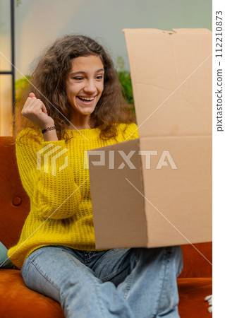 Happy child girl shopper unpacking cardboard box delivery parcel online shopping purchase at home Happy child girl shopper unpacking cardboard box delivery parcel online shopping purchase at home 112210873