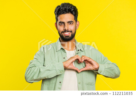 Smiling handsome man makes heart gesture demonstrates love sign expresses good feelings and sympathy 112211035
