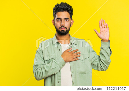 Indian man raising hand to take oath, promising to be honest and to tell truth keeping hand on chest 112211037