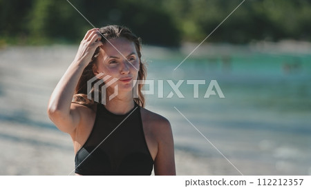 Beautiful young woman walk tropical beach. Caucasian girl in bikini enjoy nature landscape with blue sea and white sand shore. Relax on tropical island, nature summer scene. Travel, tourism, holiday 112212357