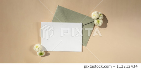 Beautiful little white flowers on postal green envelope on beige background, empty paper note copy space for text, spring time, greeting card for holiday. Flower delivery Beautiful little white flowers on postal green envelope on beige background, empty paper note copy space for text, spring time, greeting card for holiday. Flower delivery 112212434