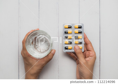 Healthcare Concept with Hand Holding Water and Pills on White Wooden Table 112214096