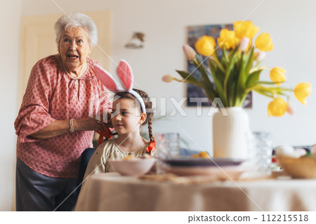 Grandmother braiding granddaughter's hair, putting ribbon on braid. Prepairing for easter lunch. Happy easter. Grandmother braiding granddaughter's hair, putting ribbon on braid. Prepairing for easter lunch. Happy easter. 112215518