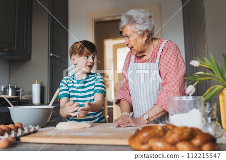 Grandmother with grandson preparing traditional easter meals, kneading dough for easter cross buns. Passing down family recipes, custom and stories. Grandmother with grandson preparing traditional easter meals, kneading dough for easter cross buns. Passing down family recipes, custom and stories. 112215547