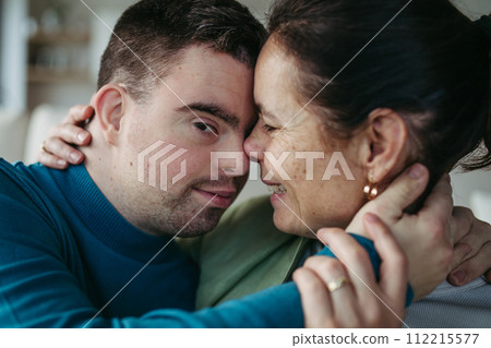 Portrait of young man with Down syndrome with his mother at home, holding, touching with foreheads. Concept of love and parenting disabled child. Banner with copyspace. Portrait of young man with Down syndrome with his mother at home, holding, touching with foreheads. Concept of love and parenting disabled child. Banner with copyspace. 112215577