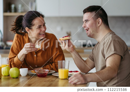 Young man with Down syndrome having breakfast with his mother at home. Morning routine for man with Down syndrome. 112215586