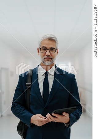Portrait of pharmaceutical sales representative in medical building, waiting for doctor, presenting new pharmaceutical product. Smiling drug rep standing in hall holding tablet. 112215597
